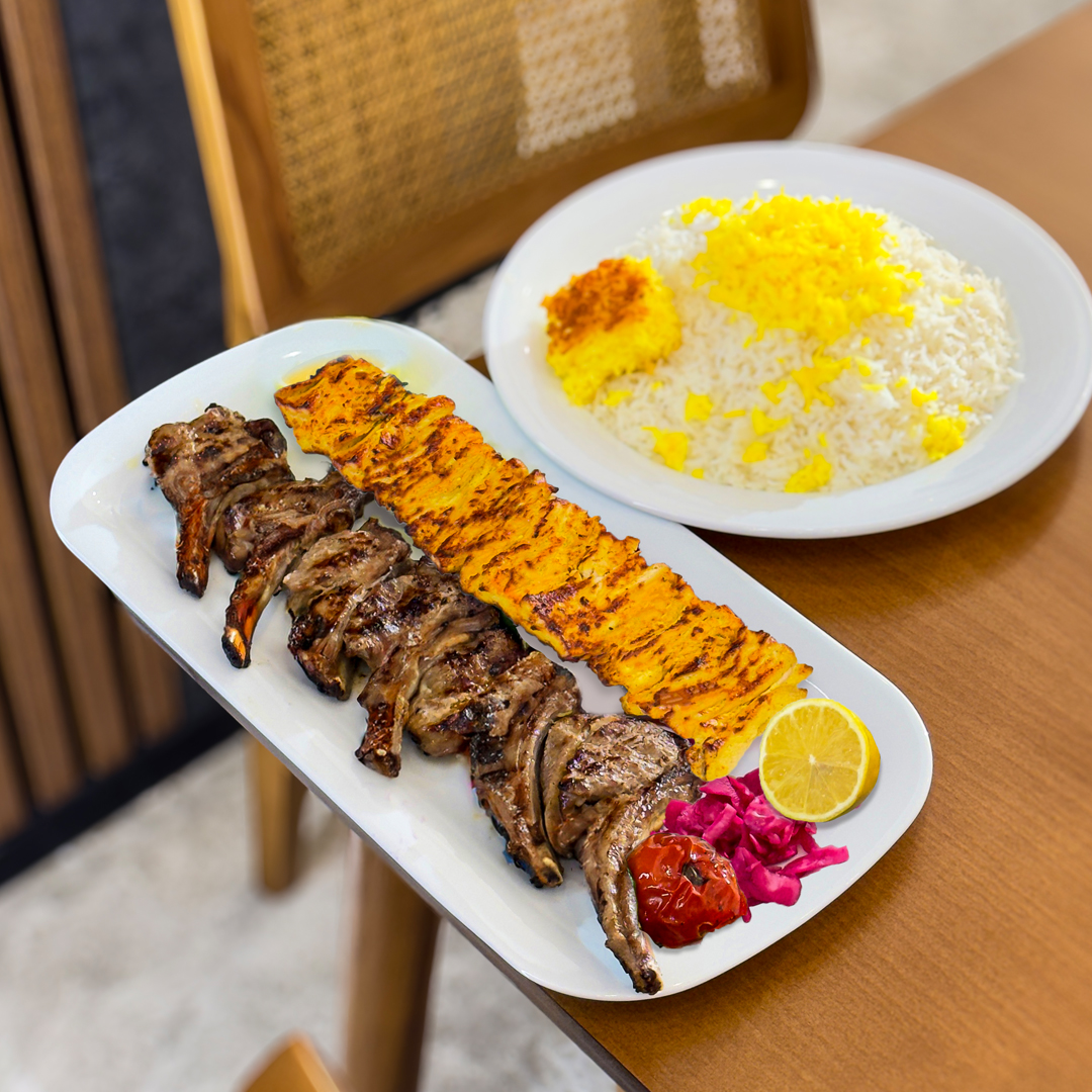 An Indian woman wearing a traditional sari wrap is using a taper to light a whole wall filled with hundreds of little oil lamps. They are illuminated and casting a bright glow over the scene; each lamp is set in its own little box within the wooden wall structure, tied with supporting pieces of bamboo. There are bunches of tiny bananas also tied to the top of the wall case.